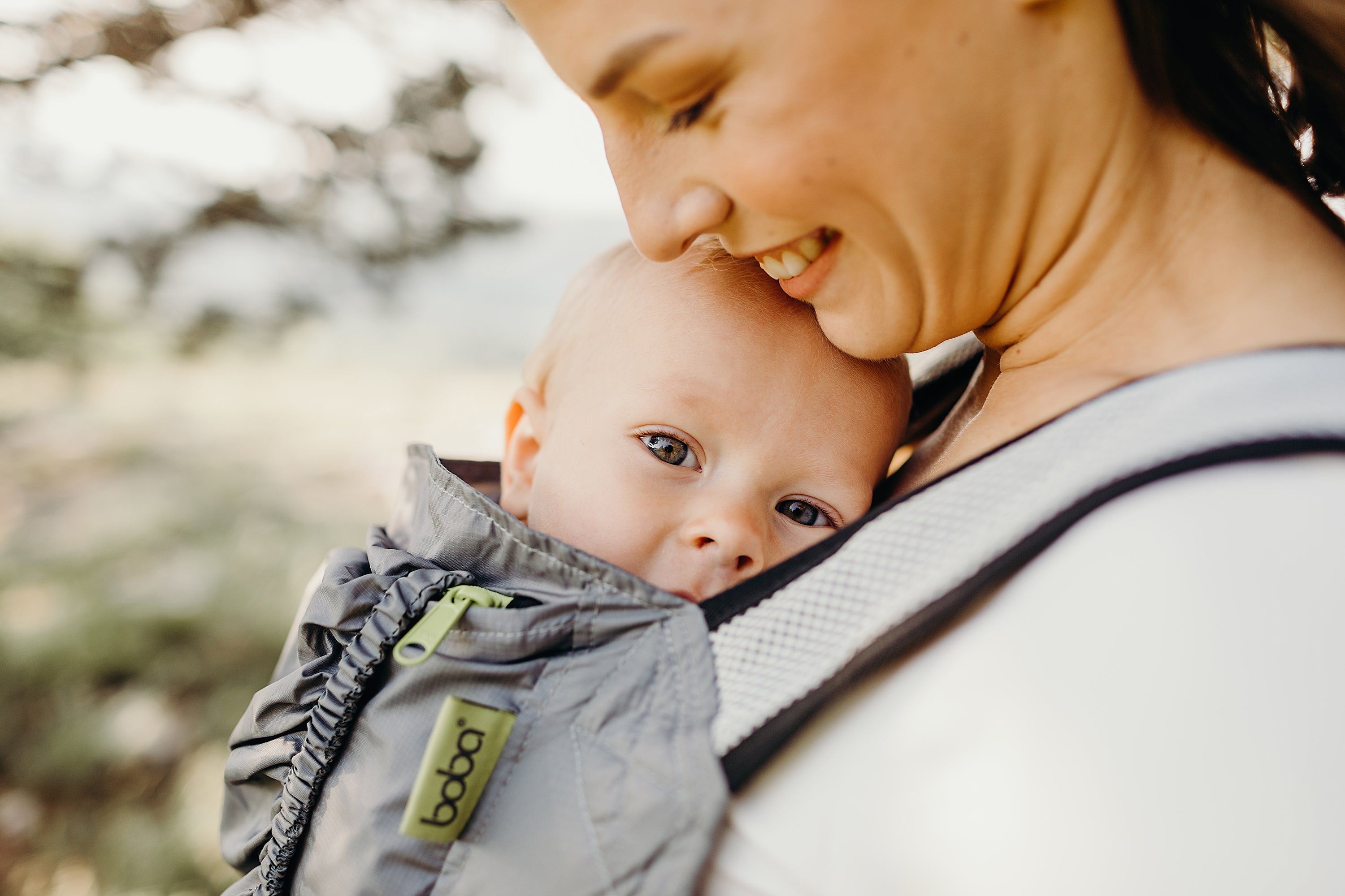 Mother looking down at her cute baby boy in the boba air gray carrier as he is chewing the mesh carrier straps