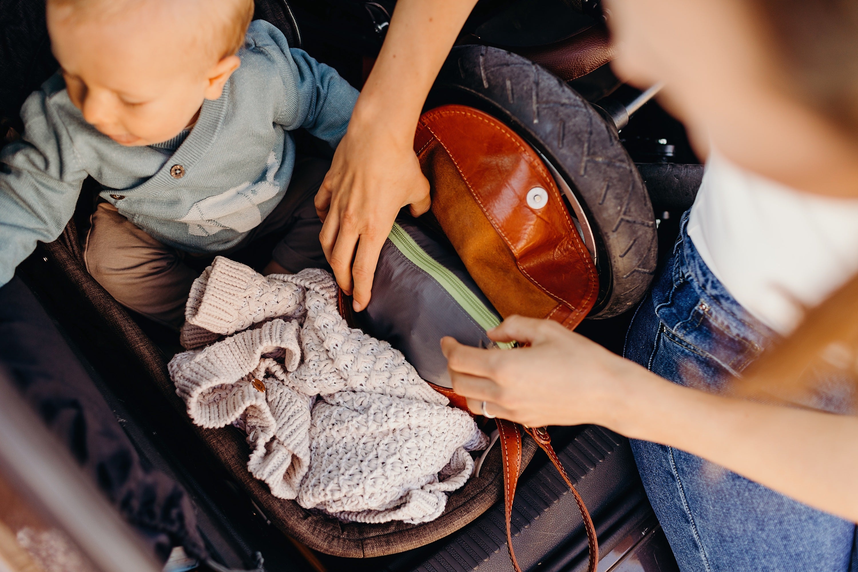 A woman with her baby sitting next to a baby stroller. She is taking the packed gray Boba Air baby carrier out of her purse.