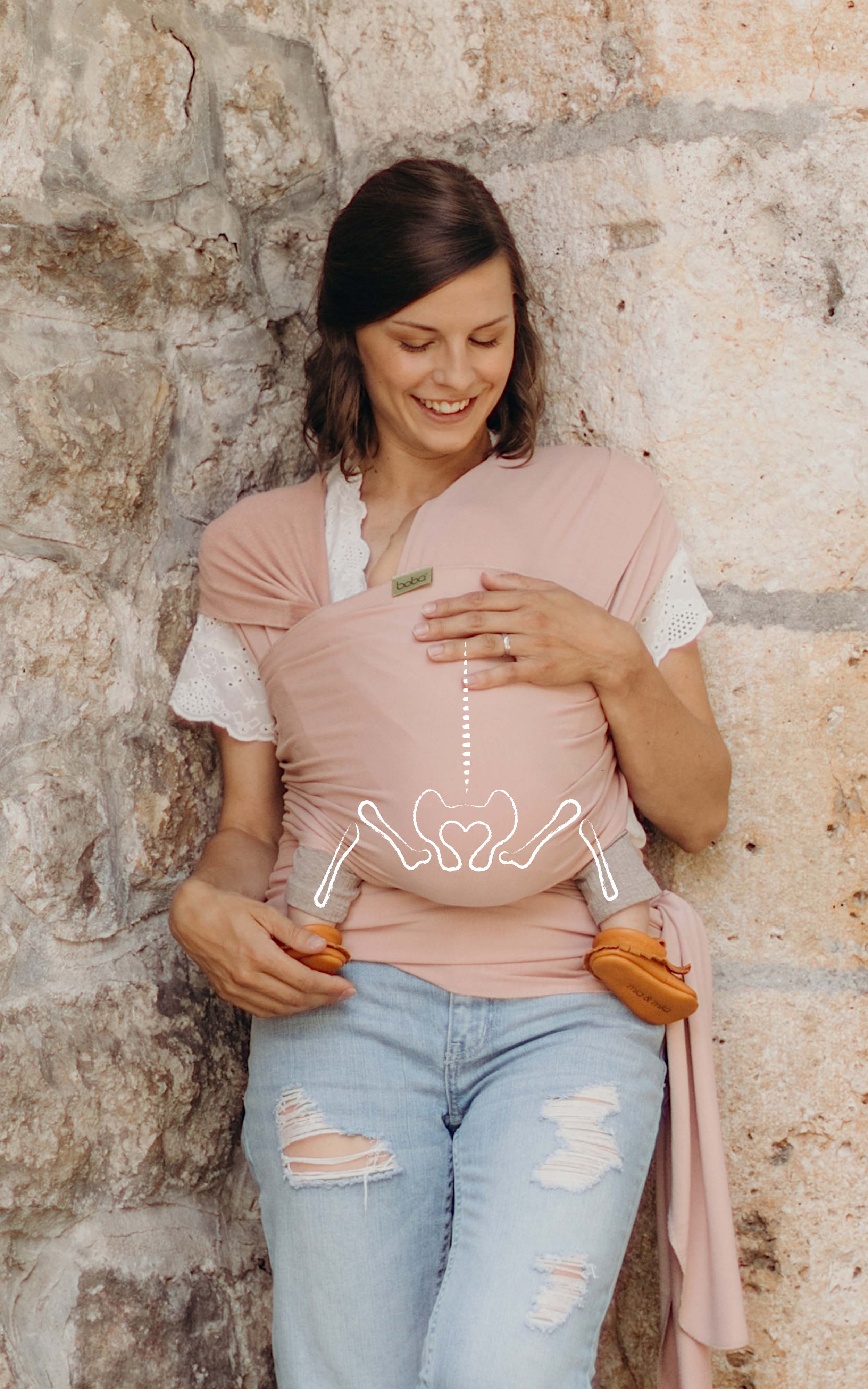 Mom wearing a white lace shirt and jeans has her sleeping baby girl in the bamboo serenity boba wrap. there is a line illustration of the baby's hips and spine in the natural ergonomic position over the photo.