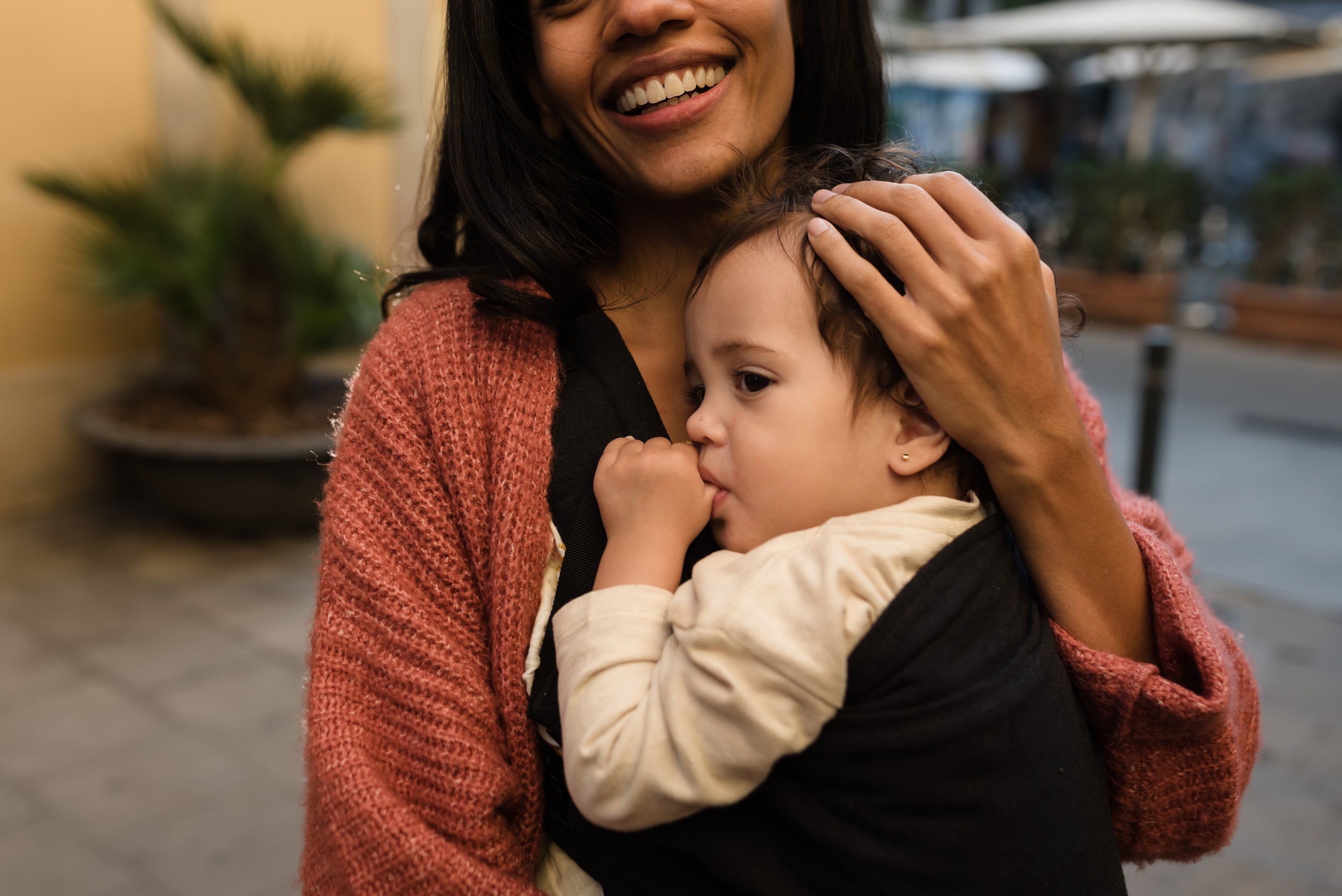 Calm and gentle mom holding her baby girl in the black x baby carrier