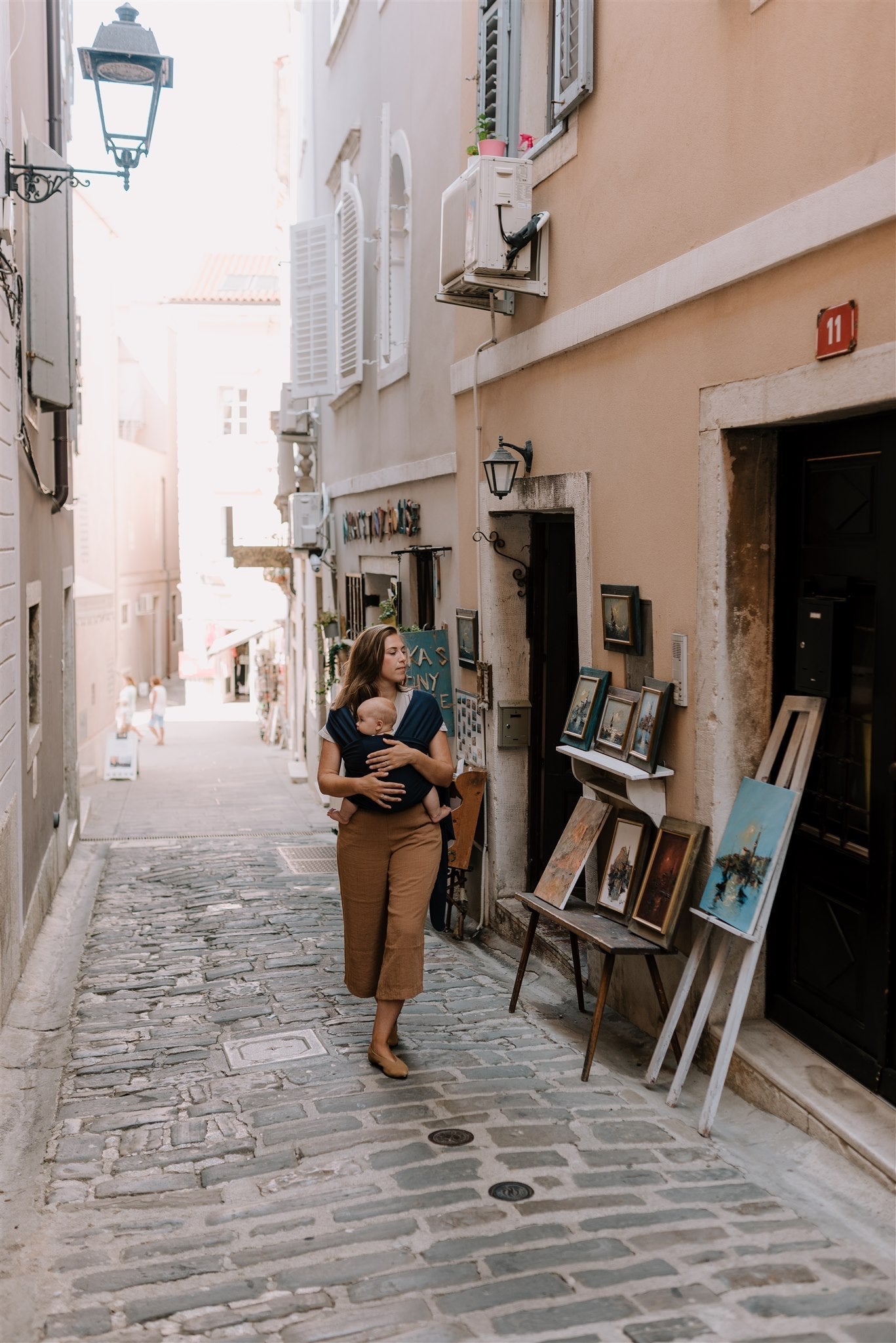 A relaxed mom strolling the streets of a seaside town with her baby in the boba navy classic wrap.