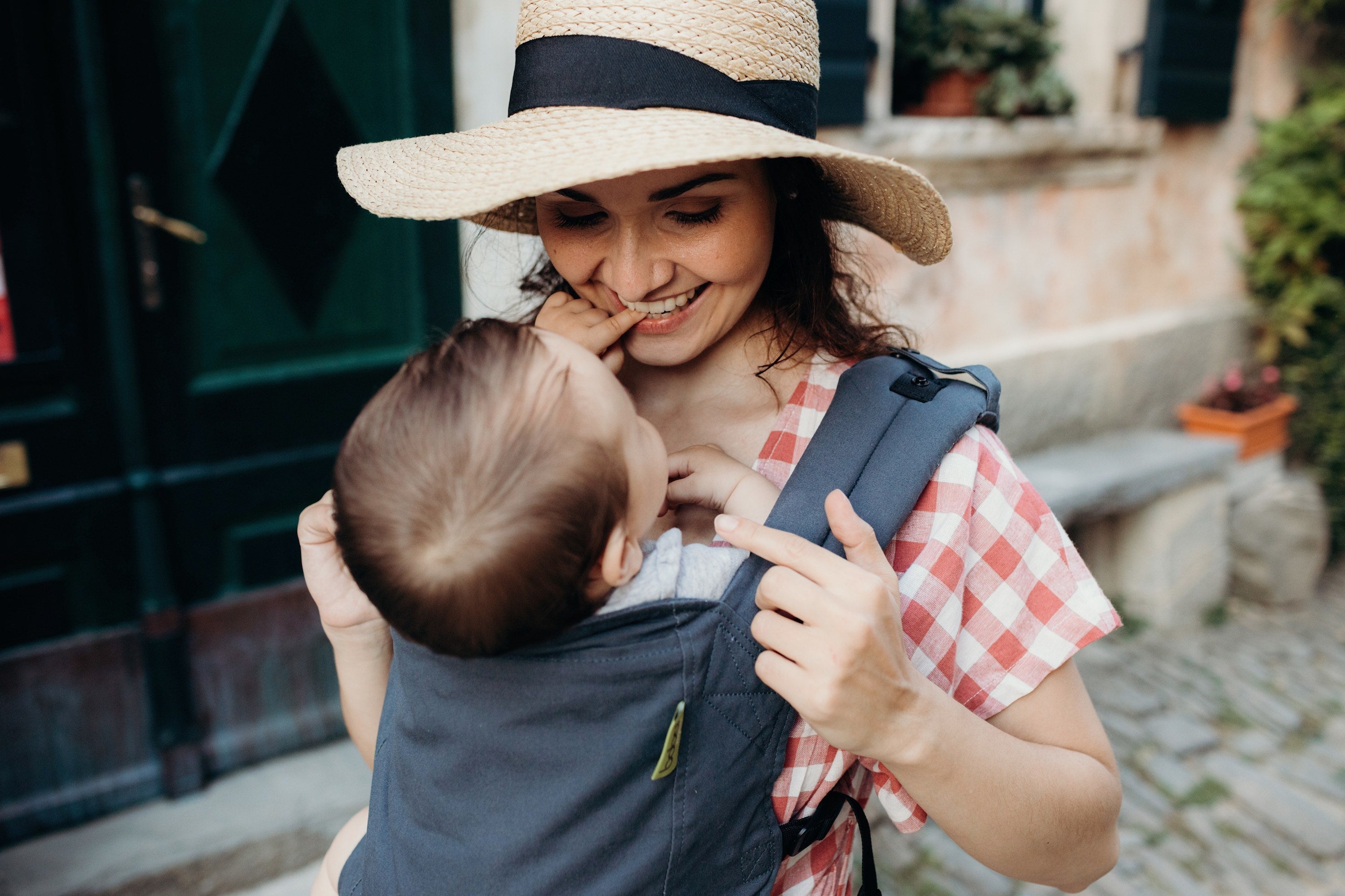 On a summer trip a smiling mom making eye contact with her baby girl that she is wearing in a charcoal gray front carry in the boba 4gs classic.