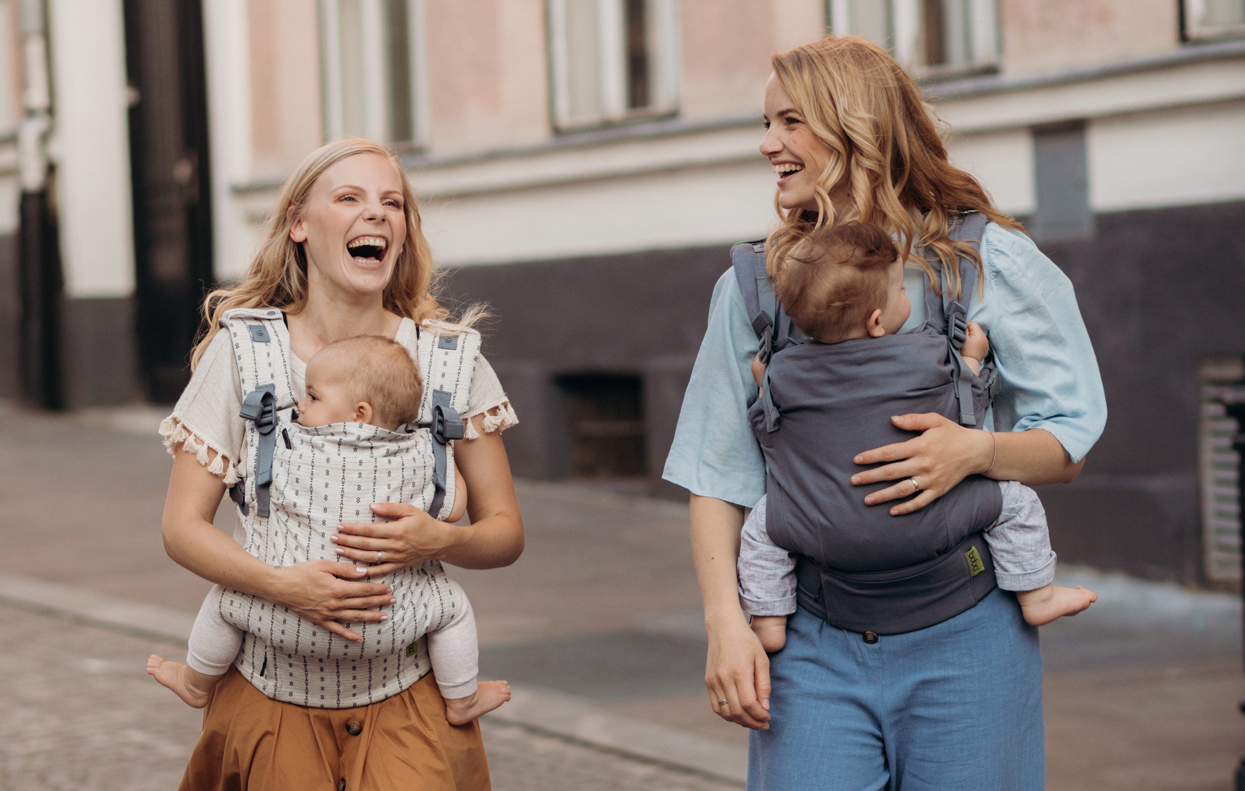 Two happy mothers with their babies in an ergonomic front carry position in the Boba X baby carrier.