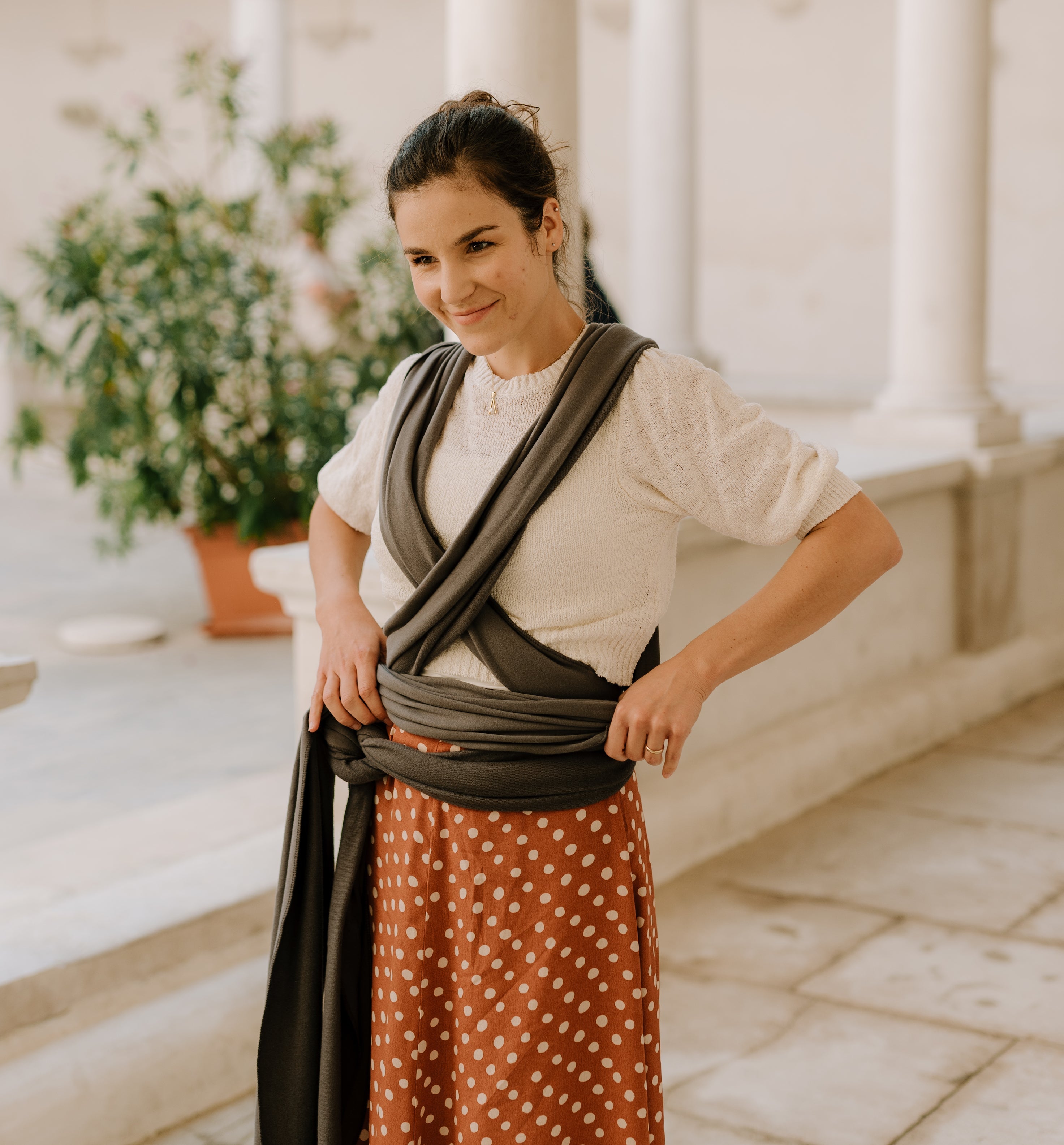 A lovely mom is standing outdoor in a summer outfit with a dark gray organic boba classic wrap already tied waiting to put her baby in an ergonomic carry.